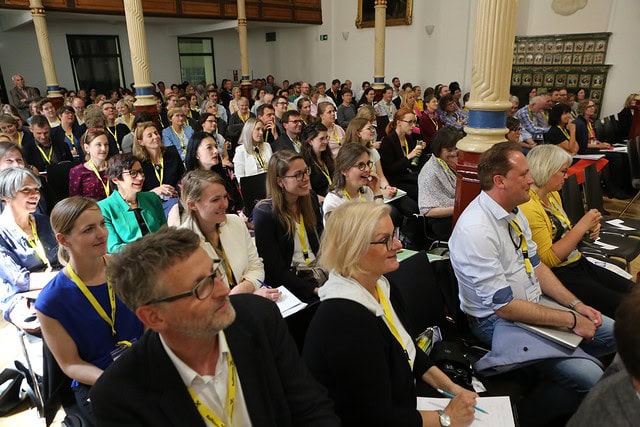 Publikum hört aufmerksam beim 3. Internationalen Kongress der IGSP zu, in einer großen Halle mit Säulen.